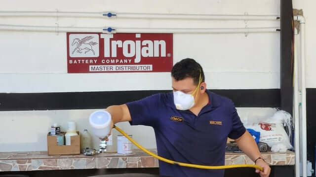 Technician spray-painting a golf cart part in the EZCARTS workshop