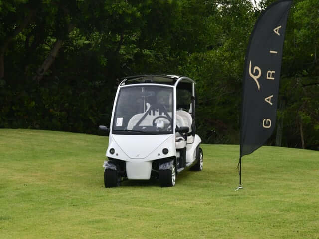 White Luxury Edition golf cart on a lawn next to a Garia flag