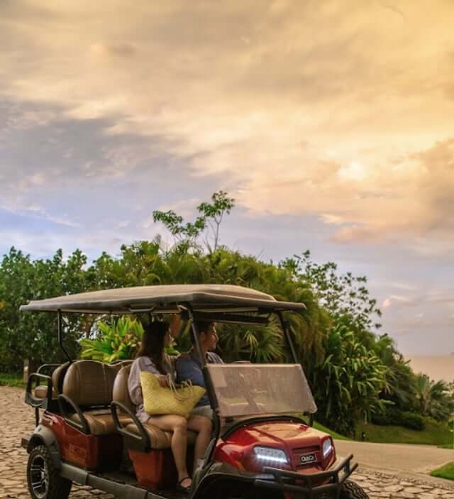 Couple driving a golf cart along a Punta Mita road at sunset